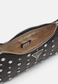 Czarna saszetka z srebrnymi ćwiekami, zamek błyskawiczny, textured materiał i beżowa podszewka z powtarzającymi się logo marki.