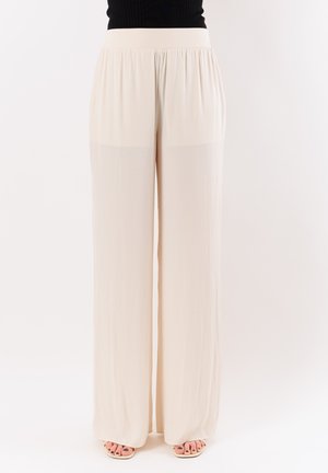 Pantaloni beige a gamba larga con vita alta elastica indossati con top nero e sandali open toe con smalto scuro sulle unghie dei piedi.