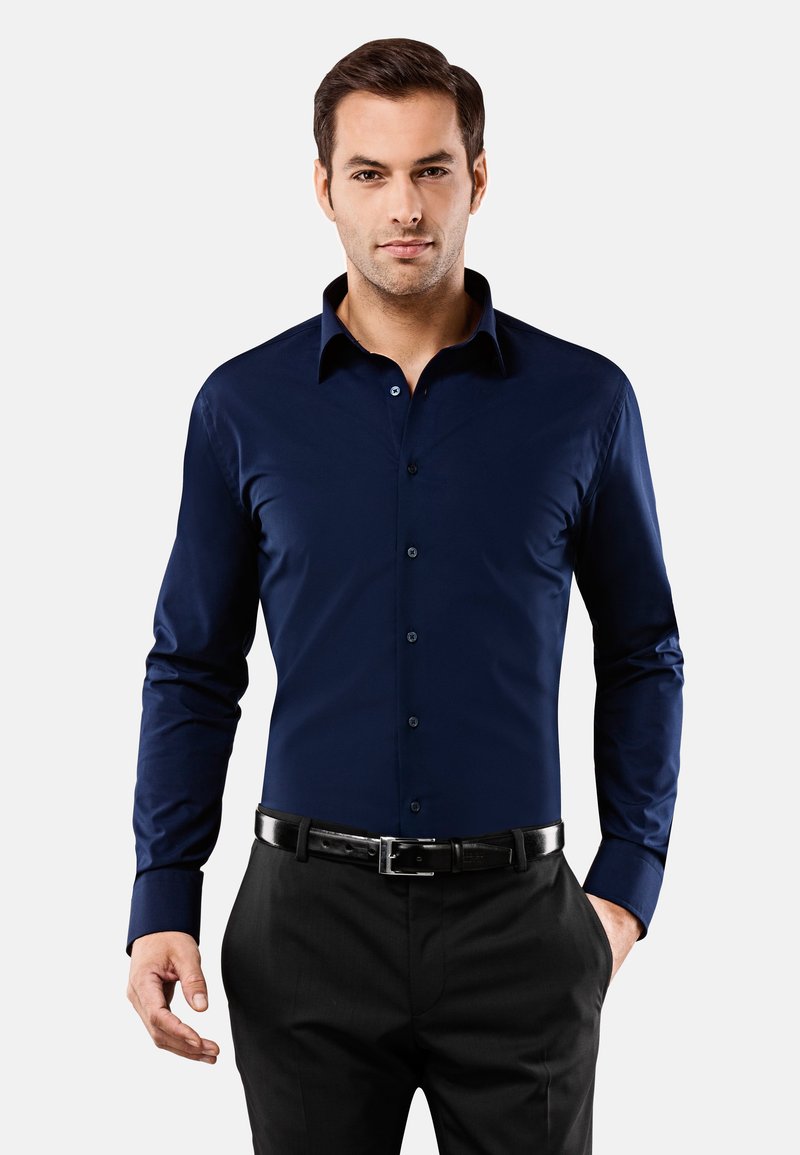 Chemise bleu marine à boutons avec des manches longues, un col pointu et une texture lisse, associée à un pantalon noir et une ceinture noire.