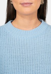 Maglione azzurro chiaro lavorato a maglia con colletto rotondo a coste e motivo a trama fine. Presenta dettagli di cucitura intricati su tutta la superficie.