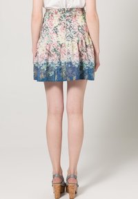 Falda con estampado floral y pinzas, que presenta un degradado de colores pastel que transiciona a azul, fabricada con una tela ligera. Combinada con sandalias de tacón de corcho.