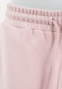 Pantalon de survêtement en tissu côtelé rose clair avec taille élastique et cordon de serrage sur un fond de haut pâle.
