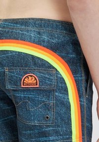I pantaloni corti in denim blu presentano una striscia multicolore a forma curva nei colori arancione, giallo e verde lungo il lato. Inclusa una tasca posteriore con un etichetta del logo.
