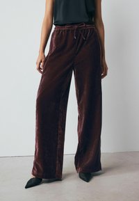 Weite Hosen aus tiefrotem Samtmaterial mit einem elastischen Bund und Zugband. Glatte Textur und fließende Silhouette.