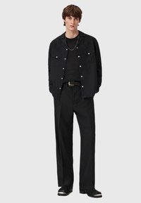 Czarna koszula z guzikami z ozdobnym przeszyciem, zestawiona z dopasowaną czarną koszulką prążkowaną i szerokimi czarnymi spodniami, dopełniona czarnymi butami.