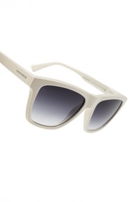 Baltas plastmasas saulesbrilles ar pārāk lielām kvadrātveida rāmjiem un pelēkiem gradienta stikliem. Uz briļļu kājiņas ir redzams "HAWKERS" logotips.