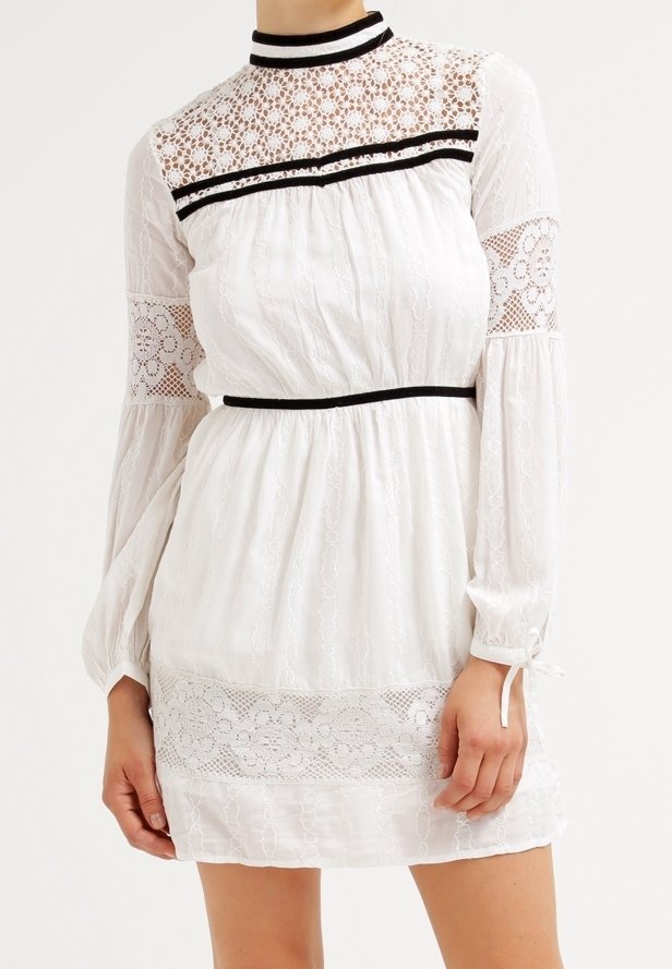 Biała sukienka z długimi rękawami, z koronkowymi akcentami, wysokim dekoltem i czarnym wykończeniem. Teksturowany materiał z warstwowym fasonem i elastycznym pasem.