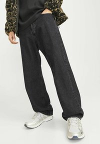Vaqueros negros de corte amplio y pierna recta, hechos de denim. Combinados con zapatillas deportivas plateadas y una blusa negra texturizada.