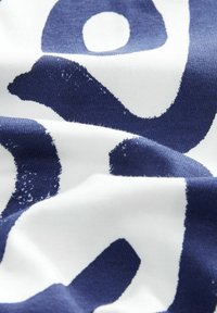 Tejido de algodón con un audaz patrón abstracto en azul marino y blanco. Sensación suave y texturizada con costuras visibles y ligero deshilachado en algunas áreas.