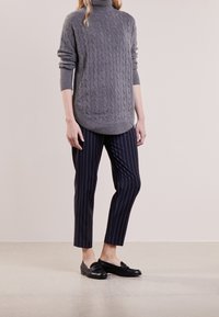 Suéter de cuello alto de punto trenzado gris con dobladillo redondeado, combinado con pantalones tapered a rayas en azul marino y mocasines negros. Textura suave, diseño casual.