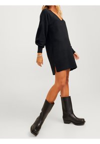 Vestito lungo nero in maglia con scollo a V, maniche a palloncino, spacchi laterali e polsini a costine. Abbinato a stivali neri con tacco alto fino al ginocchio.