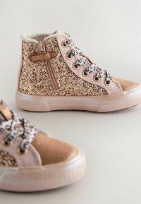 Baskets montantes en rose gold pailleté avec une fermeture éclair sur le côté, doublure en crème douce et lacets à motifs. À l'avant, un capuchon en daim et une semelle texturée.