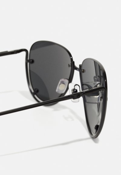 Lunettes de soleil noires avec une monture en métal, des verres ovales et des plaquettes de nez ajustables. Les verres sont gris foncé avec une surface lisse et réfléchissante.