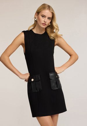 Zwart mouwloos jurk met een aansluitende silhouet, voorzien van twee voorkruike zakken met glanzende gouden accenten en een gladde stofstructuur.