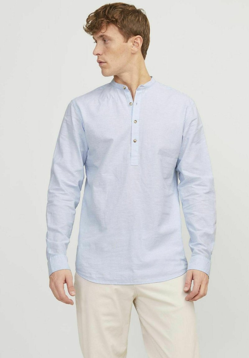 Camicia a maniche lunghe blu chiaro con collo henley, caratterizzata da tre bottoni metallici e un sottile motivo a righe. Tessuto morbido e liscio.