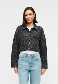 Μαύρο κοντό τζιν μπουφάν με γεωμετρικό σχέδιο, κλείσιμο με κουμπιά και γιακά. Συνδυασμένο με ανοιχτό μπλε τζιν ψηλόμεσο.