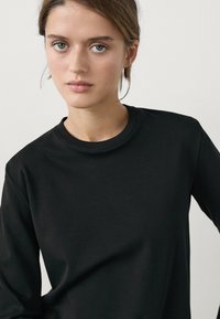 Black long-sleeve top with a rounded neckline. Smooth fabric texture, slim fit, and minimal design with no visible patterns or accents.
