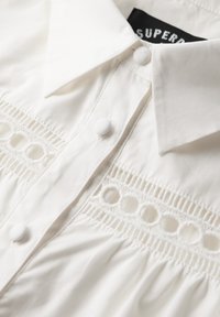 Camicia bianca con colletto, bordature testurizzate con ritagli circolari e tessuto morbido con dettagli arricciati.