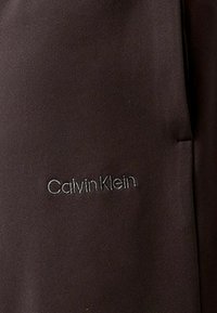 Prenda de tela negra con una textura suave, que presenta un discreto logotipo bordado de "Calvin Klein", situado en la parte inferior derecha.