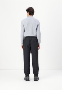 Cămașă gri cu mânecă lungă, pantaloni negri cu talie elastică și o buzunar, și sneakers negri. Material neted, croială lejeră și design cu picior strâns.