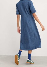 Denim shirt dress with short sleeves, mid-length cut, and a button-down collar. Worn with green sneakers and blue socks.
