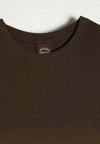 Brązowy sportowy t-shirt z prążkowanym dekoltem i wytłoczonym logo "Diverse Athletics" na piersi. Gładka tekstura, dopasowany krój.