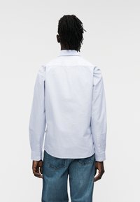 Μακρυμάνικο πουκάμισο ανοιχτού μπλε με κλασικό γιακά, μανσέτες με κουμπιά και απαλό βαμβακερό ύφασμα. Διαθέτει ευθεία ραφή στην πλάτη και μινιμαλιστικό στιλ.