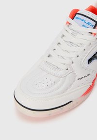 Białe skórzane sneakersy z perforowanymi detalami, sznurowanym przodem, czarnymi i czerwonymi akcentami oraz półprzezroczystą podeszwą z kolorowymi drobinkami.