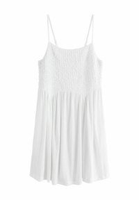 Robe blanche sans manches avec un corsage smocké texturé et une jupe fluide froncée. Fabriquée en tissu léger, elle présente des bretelles fines.