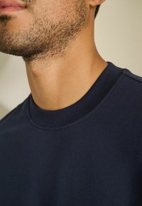 Navyblauwe sweatshirt met ronde hals, gemaakt van zachte stof met een gladde textuur; heeft subtiele naaddetails bij de kraag.