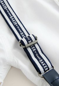 Primo piano di una cinghia di tessuto a righe blu navy e bianche con regolatore in metallo e testo "BAKER BY TED BAKER" su un capo bianco.