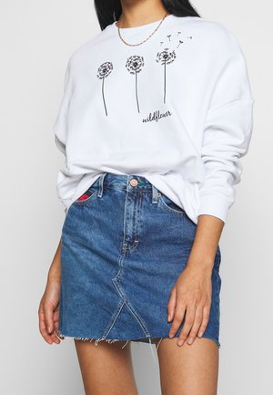 Witte sweatshirt met zwart paardenbloem-graphic en "wildflower" tekst, gecombineerd met een blauwe denim rok met een voorkantsplit en rafelige zoom.