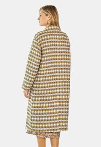 Długi płaszcz w kratę w odcieniach żółtego, brązowego i białego. Wykonany z teksturowanej tkaniny, z kołnierzem i luźnym krojem.