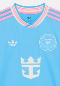 Svetlomodrý futbalový dres s ružovými a bielymi pásikmi na golieri a rukávoch. Na prednej strane sa nachádza biele logo a emblém. Textúrovaná tkanina.