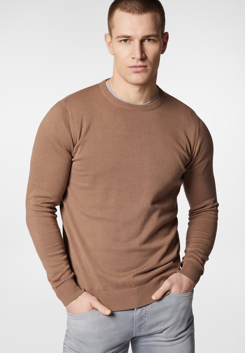 Brązowy sweter dziany z okrągłym dekoltem i ściągaczami, o dopasowanym kroju i gładkiej fakturze. Noszony z jasnoszarymi spodniami.