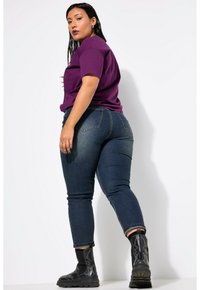 Camiseta corta de manga corta en color púrpura con un corte relajado, combinada con jeans ajustados de color azul oscuro y botas tobilleras negras con suela texturizada.