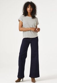 Top a rayas de mangas cortas en color crema y negro, combinado con vaqueros de pierna ancha en azul oscuro. La modelo lleva botas de tacón marrones.