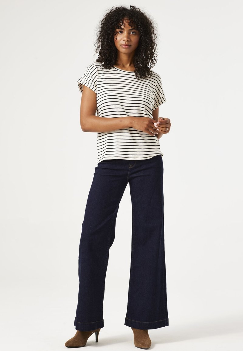 Top a rayas de mangas cortas en color crema y negro, combinado con vaqueros de pierna ancha en azul oscuro. La modelo lleva botas de tacón marrones.