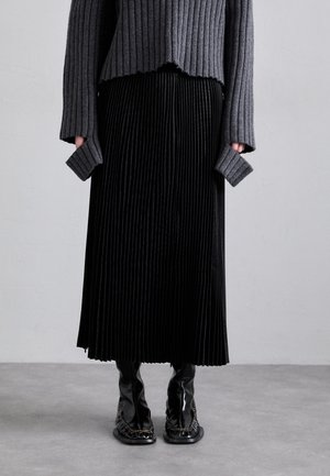Gray ribbed sweater with frayed hem paired with a black pleated skirt. Glossy black ankle boots with an intricate trim detail.
