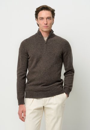 Brauner Pullover mit Reißverschluss am Hals, mit geripptem Saum und Bündchen, aus weichem Stoff. Stilisiert über einem hellen Hemd, kombiniert mit cremefarbenen Hosen.