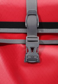 Borsa impermeabile rossa con superficie testurizzata, spallacci grigi e una robusta fibbia grigia con branding. Include una striscia accentata nera.
