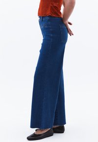 Džínové kalhoty s vysokým pasem a širokými nohavicemi v modré barvě se třepeným lemem. Mají zadní kapsy a zapínání na knoflík v pase. Hladká textura.