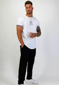 Vit t-shirt med blommönstrade ärmar och svarta byxor. T-shirten har ett stiliserat "A" på framsidan. Bärs med vita sneakers.