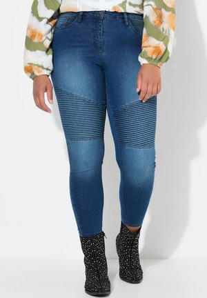 Jean skinny en denim bleu tapered avec des accents côtelés sur les cuisses, taille haute et décoloration subtile. Associé à des bottines à paillettes noires.