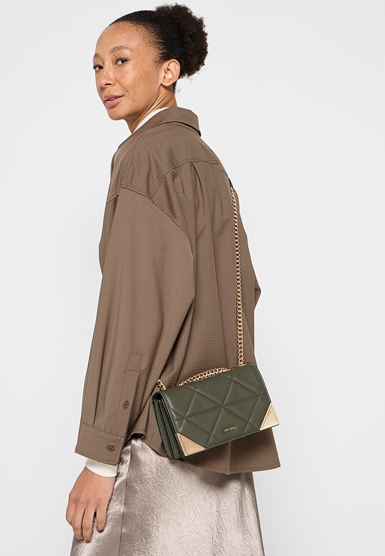 Sac à main en cuir matelassé vert avec des accents en métal doré, doté d'une bandoulière en chaîne et de détails en forme de triangle, présenté sur un fond uni.