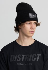 Beanie nero lavorato a maglia con risvolto, dotato di una toppa rettangolare con testo bianco. T-shirt nera con stampa grafica nera opaca.