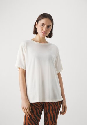 Camisa de manga corta color crema con escote redondo, hecha de una tela suave, combinada con leggings a rayas marrones y negros.