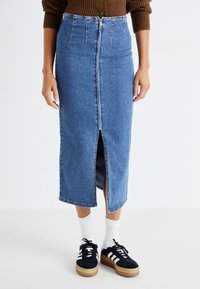 Denim midi krilo v svetlo modri barvi s sprednjim razporkom, visokim pasom in zadnjimi žepi. Ujemite z črnimi supergami in belimi nogavicami.