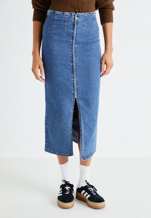 Jupe midi en denim bleu clair avec une fente avant, taille haute et poches arrière. Associée à des baskets noires et des chaussettes blanches.