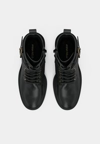 Μαύρα δερμάτινα μποτάκια έως τον αστράγαλο με στρογγυλές μύτες, κορδόνια μπροστά και χρυσές οπές. Περιλαμβάνουν λεπτομέρεια με πόρπη στο πλάι και λεία υφή.